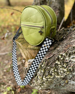 Green round bag with a checkered strap on a tree branch outdoors