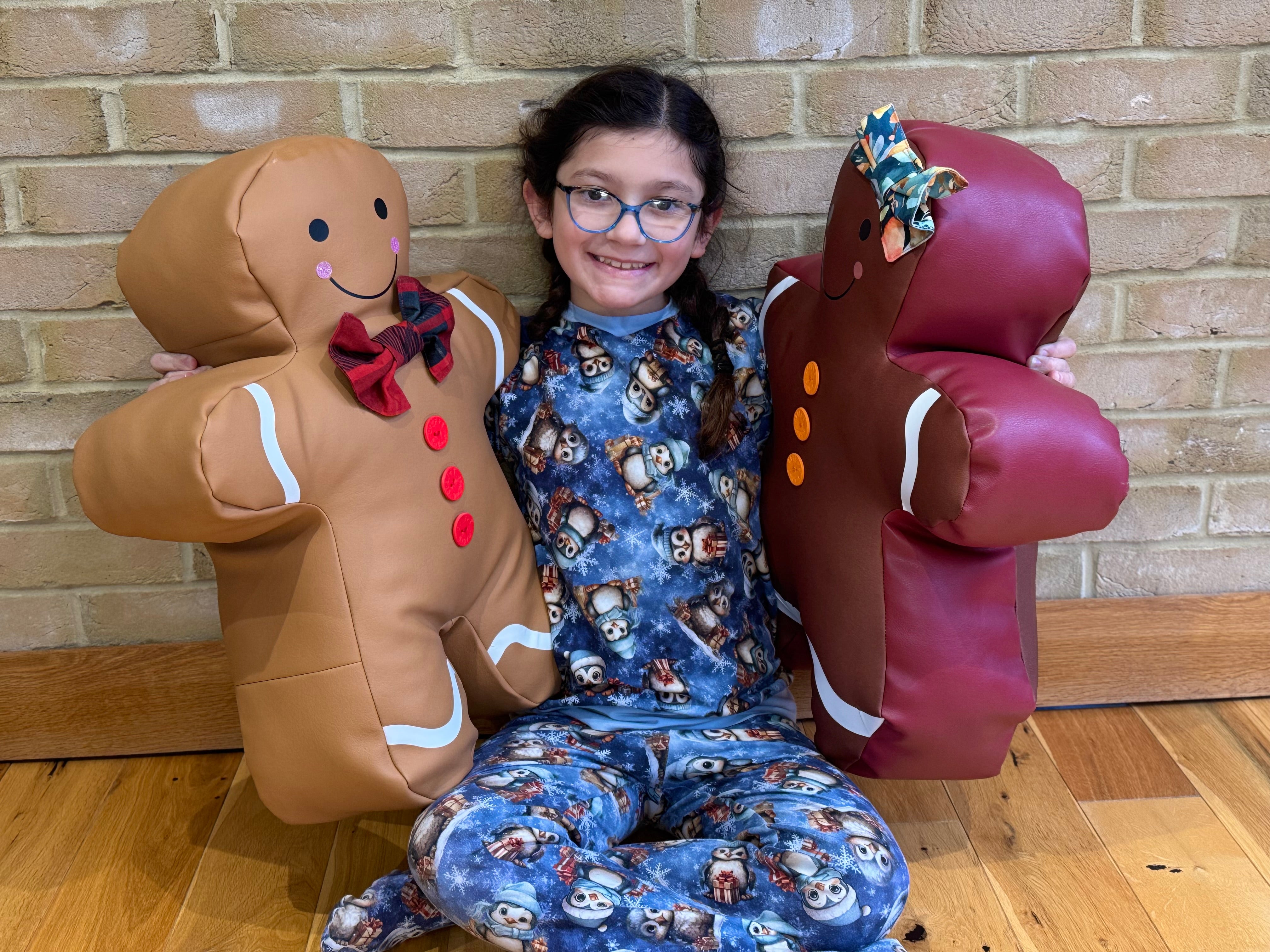 Child in pajamas with gingerbread man and woman against a brick wall.