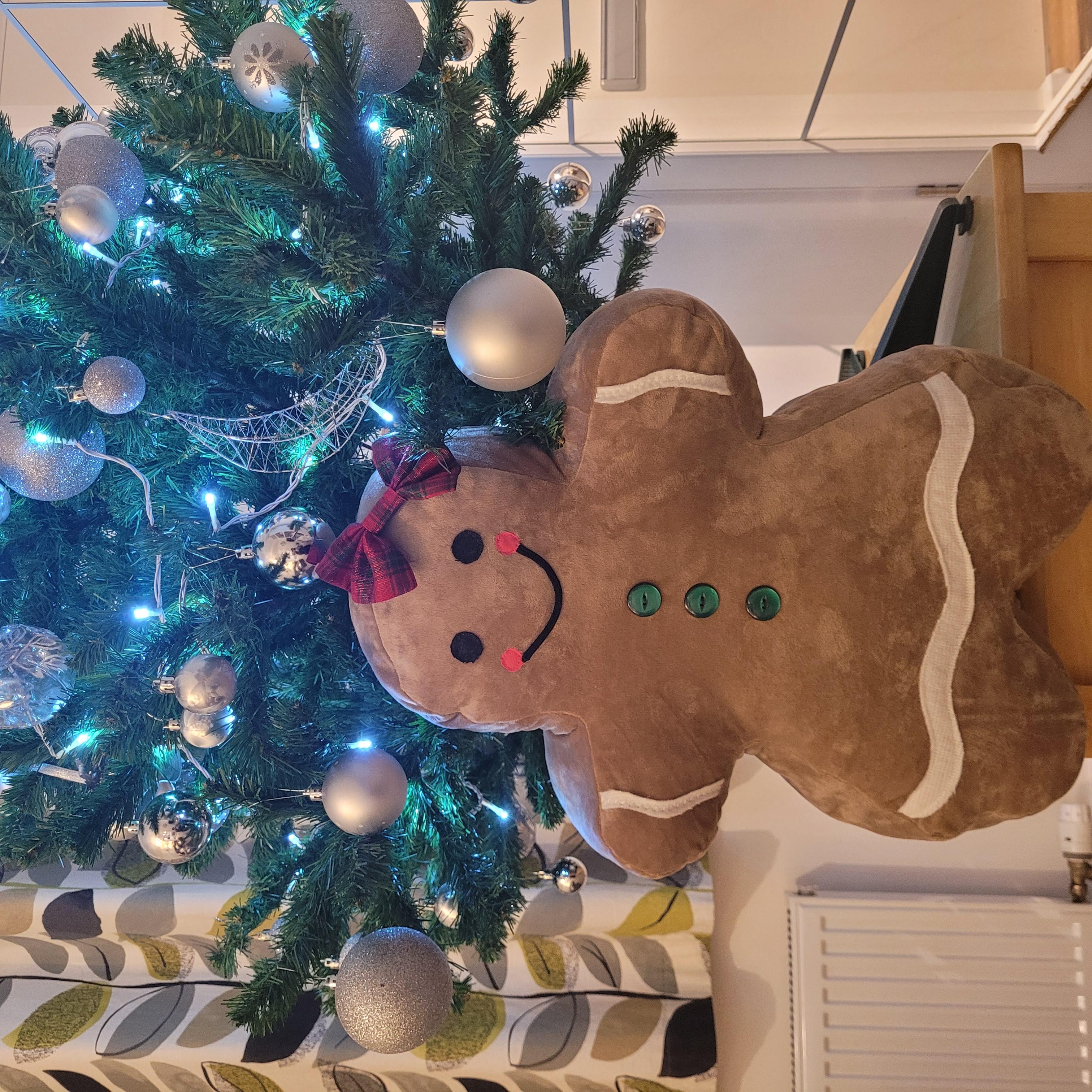 Jolly Gingerbread People Pillow styled beside a Christmas tree for holiday decorating.
