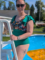 Woman in a green swimsuit standing by a pool with sunglasses on