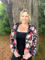 Woman outside modeling a bright floral athleisure hooded jacket with zip closure, kangaroo pocket detail, and thumbhole cuffs. Easy pdf sewing pattern.