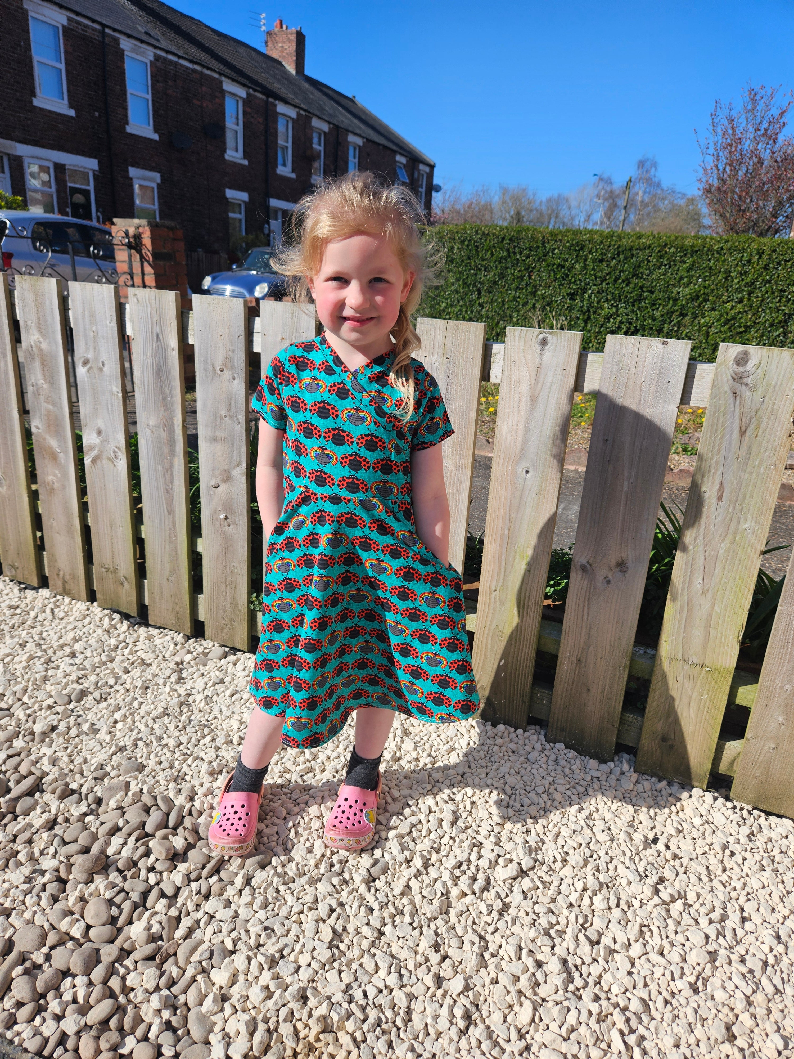 Ladybug fabric dress with faux wrap bodice and short sleeves. 1/2 Circle skirt with pockets. Toddler to teen sewing pattern.