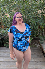 Woman in a swimsuit standing by a pool with trees and a building in the background