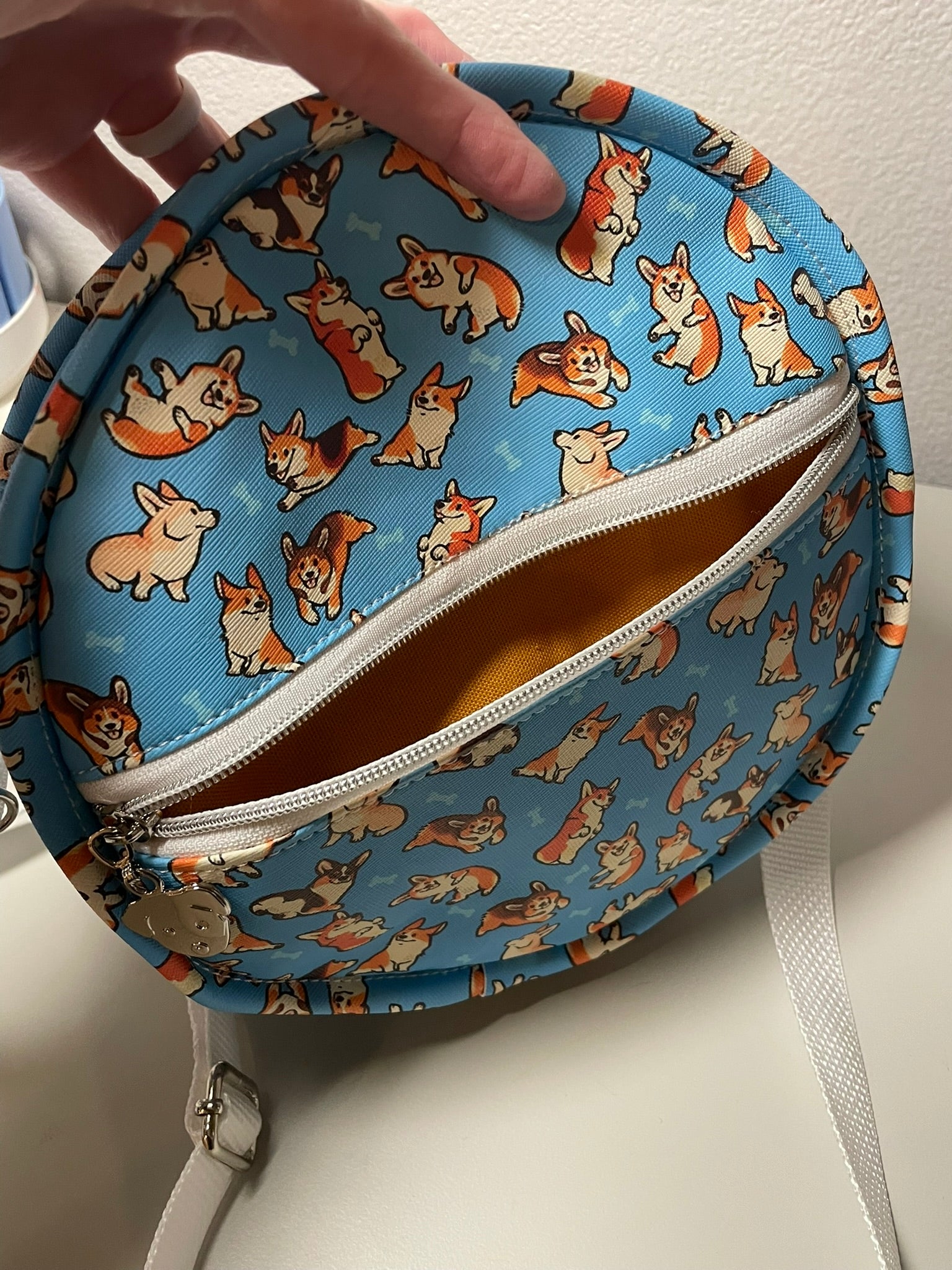 Round blue pouch with corgi pattern held by a hand on a white surface