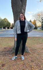Person wearing a cropped gray sweater cardigan over a black top and leggings. 
