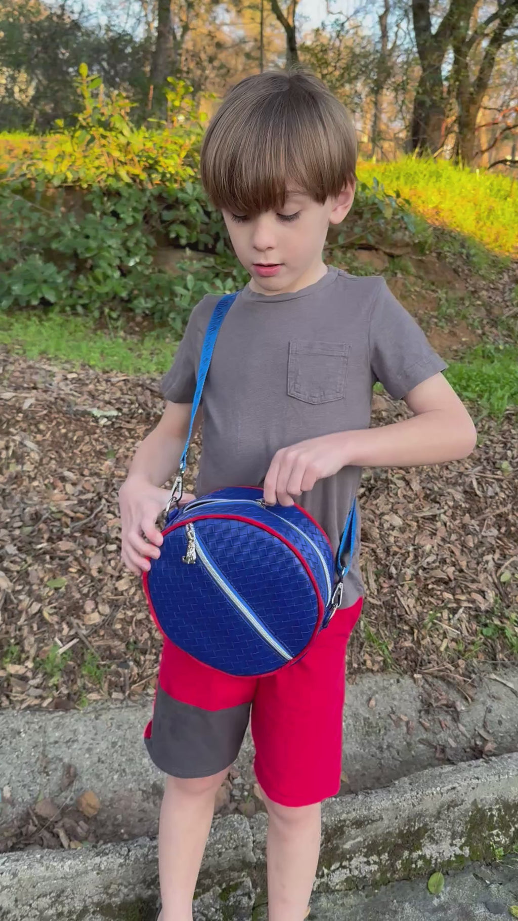 Boy wearing a Small Ellie Round Bag in blue faux leather with a paw print strap.