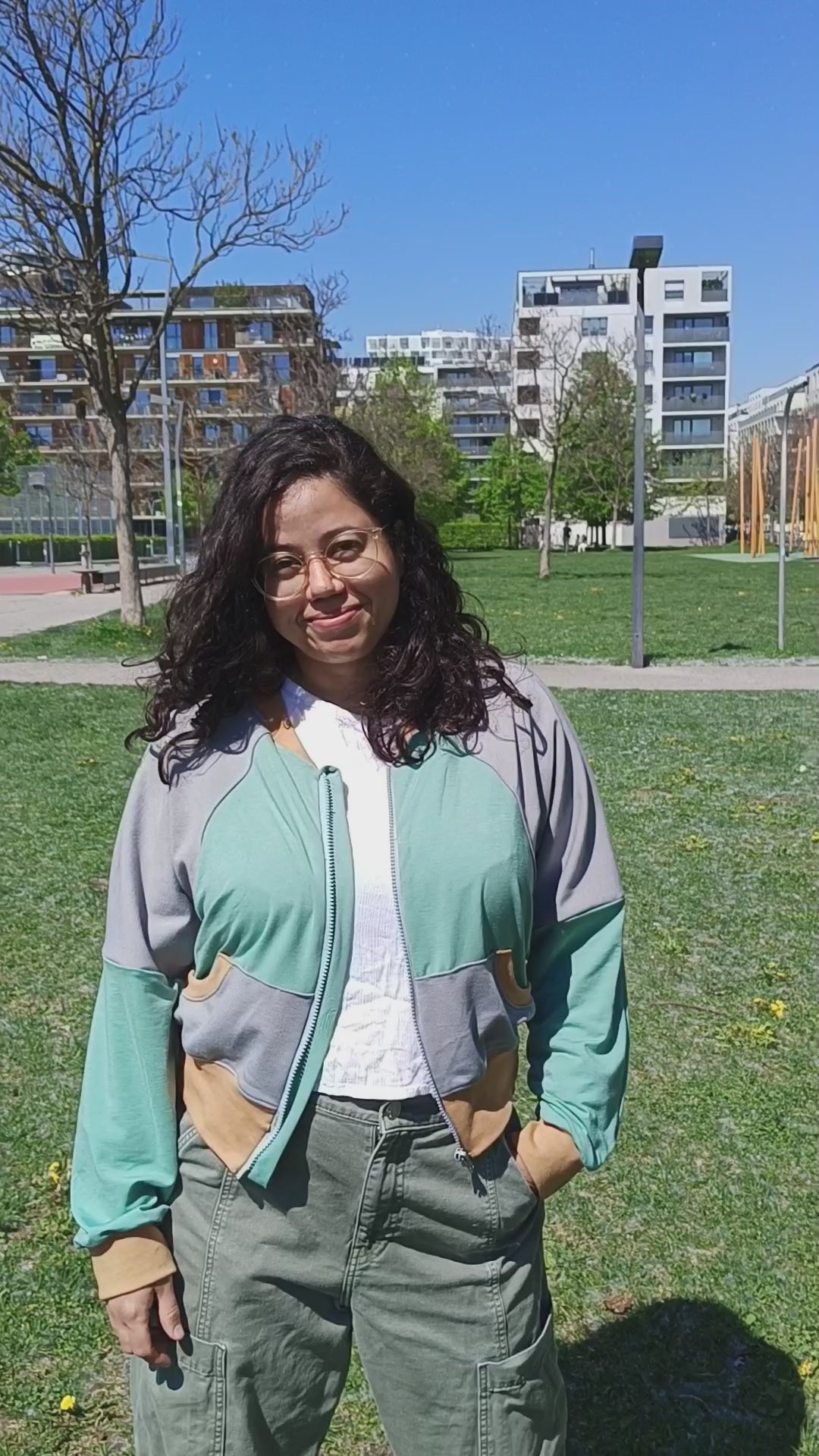 Woman outside modeling a color-blocked raglan bomber jacket with zip closure, kangaroo pocket detail, and cuffs. Easy pdf sewing pattern.