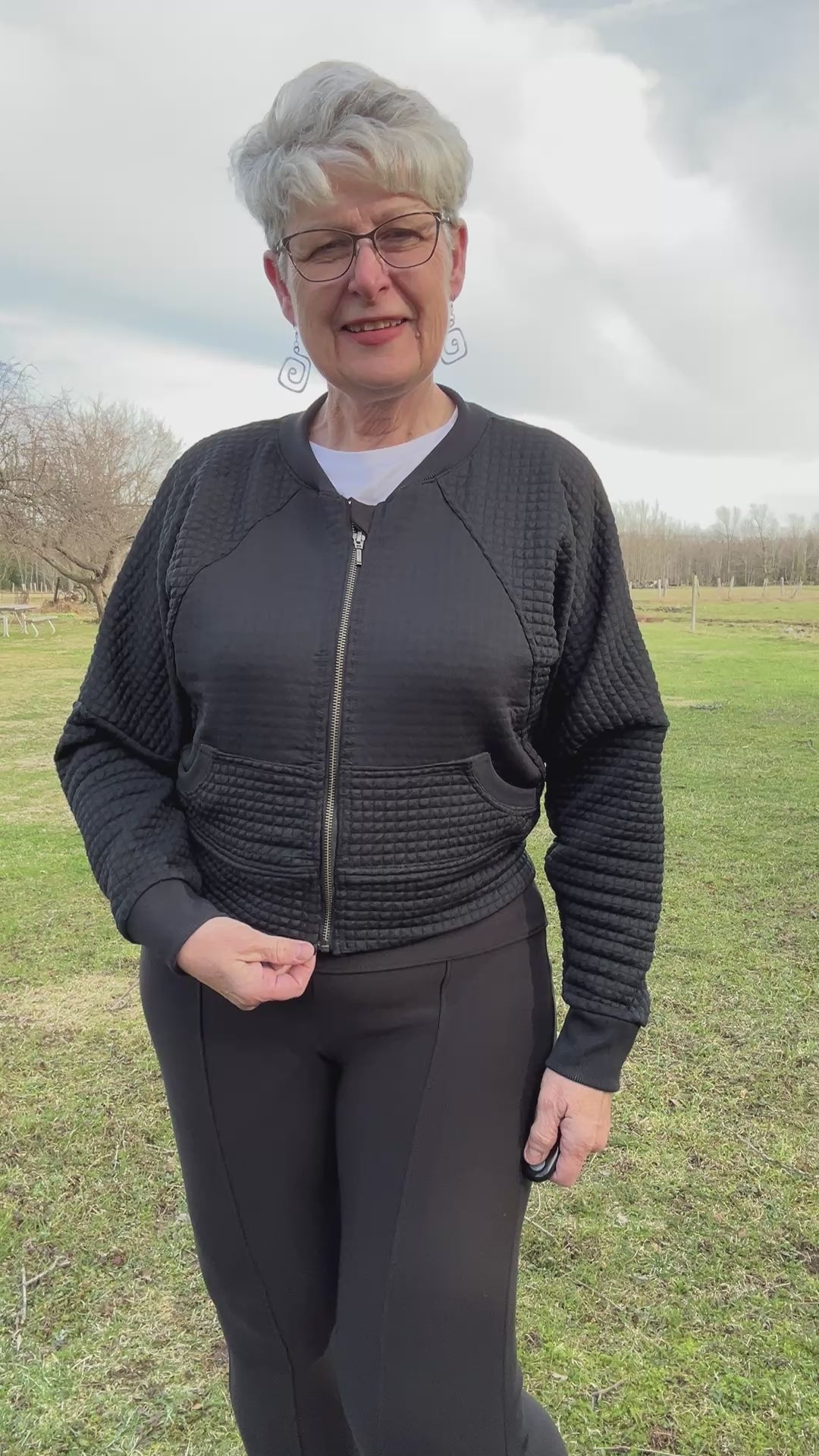 Woman outside in a park modeling a black textured fabric knit bomber jacket with zip closure. Athletic Cropped version. Ellie and Mac PDF sewing patterns.
