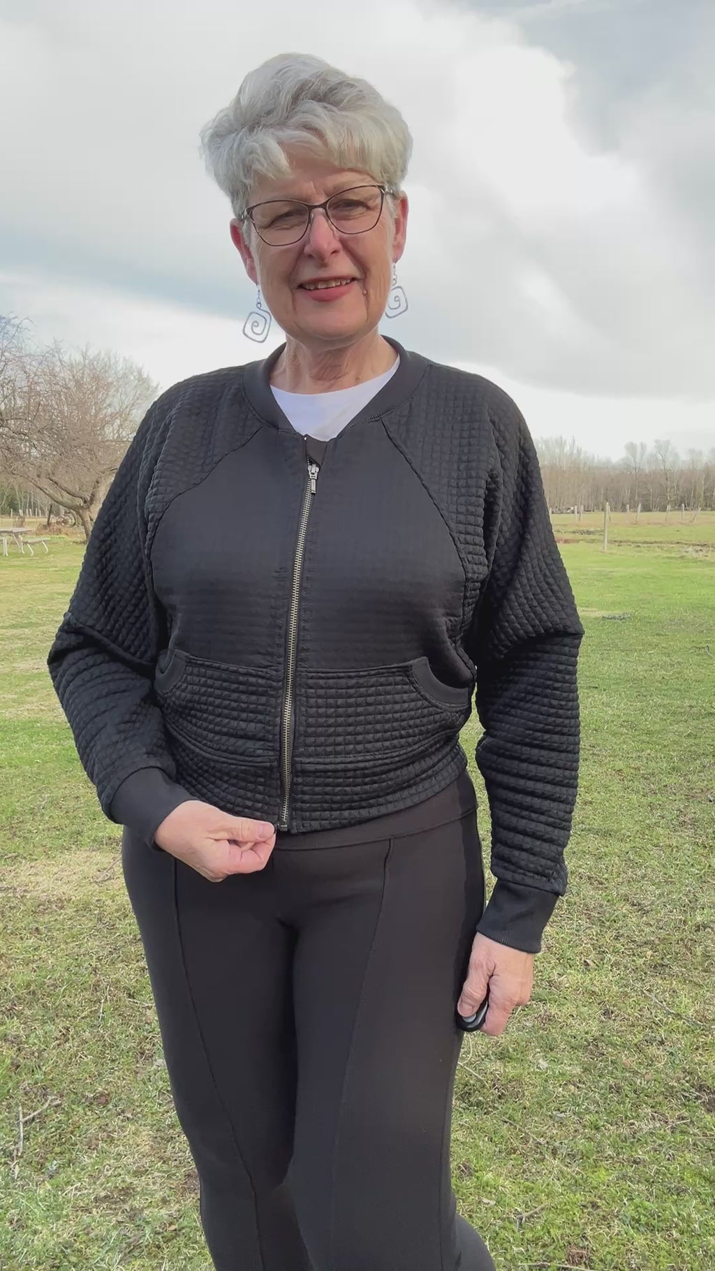 Woman outside in a park modeling a black textured fabric knit bomber jacket with zip closure. Athletic Cropped version. Ellie and Mac PDF sewing patterns.