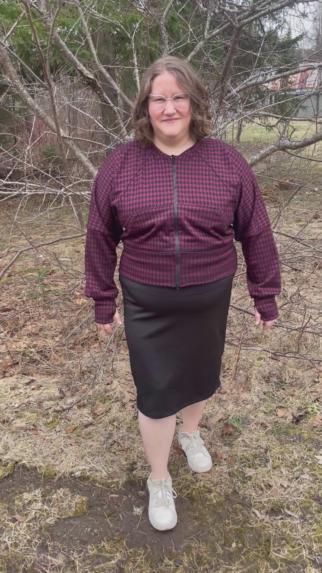 Woman outside modeling a burgundy and black houndstooth athletic bomber jacket with zip closure, kangaroo pocket detail, and thumbhole cuffs. Easy pdf sewing pattern.