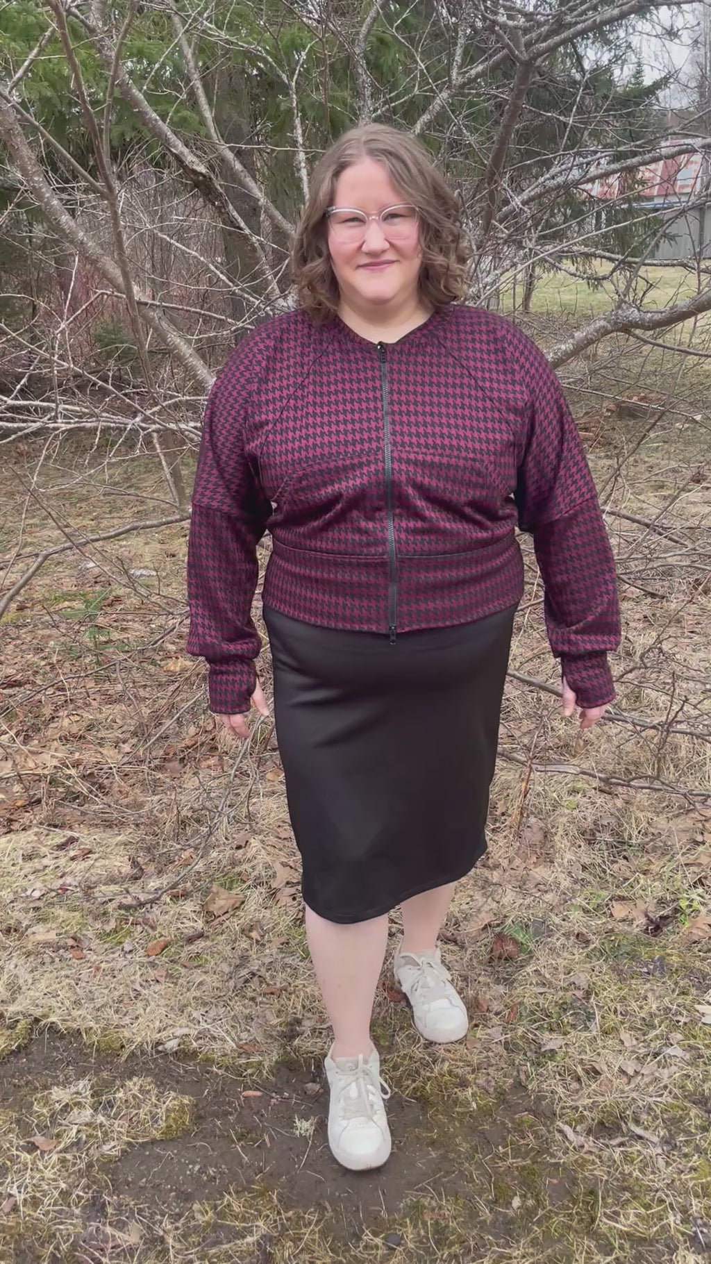 Woman outside modeling a burgundy and black houndstooth athletic bomber jacket with zip closure, kangaroo pocket detail, and thumbhole cuffs. Easy pdf sewing pattern.