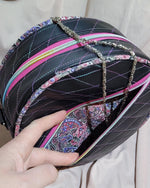 Hand holding a black quilted handbag with colorful accents on a beige fabric background