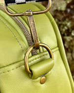 Close-up of a green handbag with a checkered strap and brass hardware.