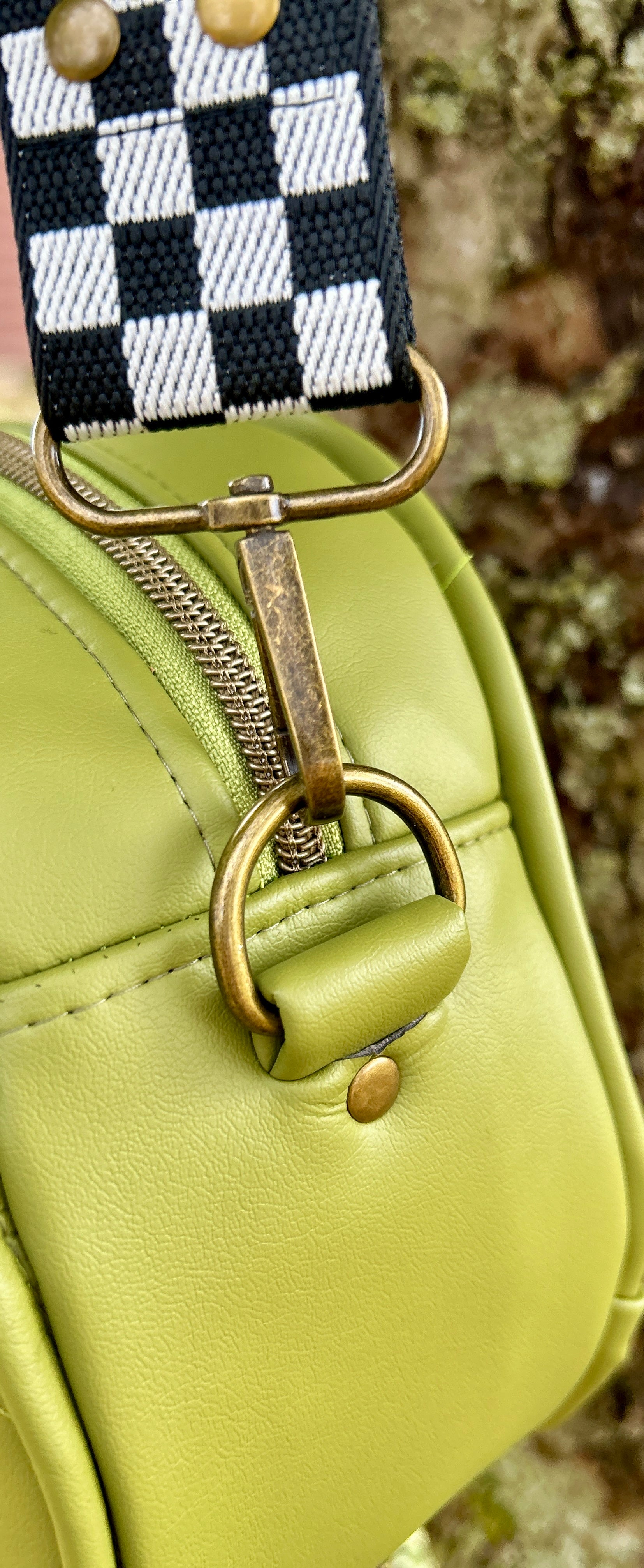 Close-up of a green handbag with a checkered strap and brass hardware.