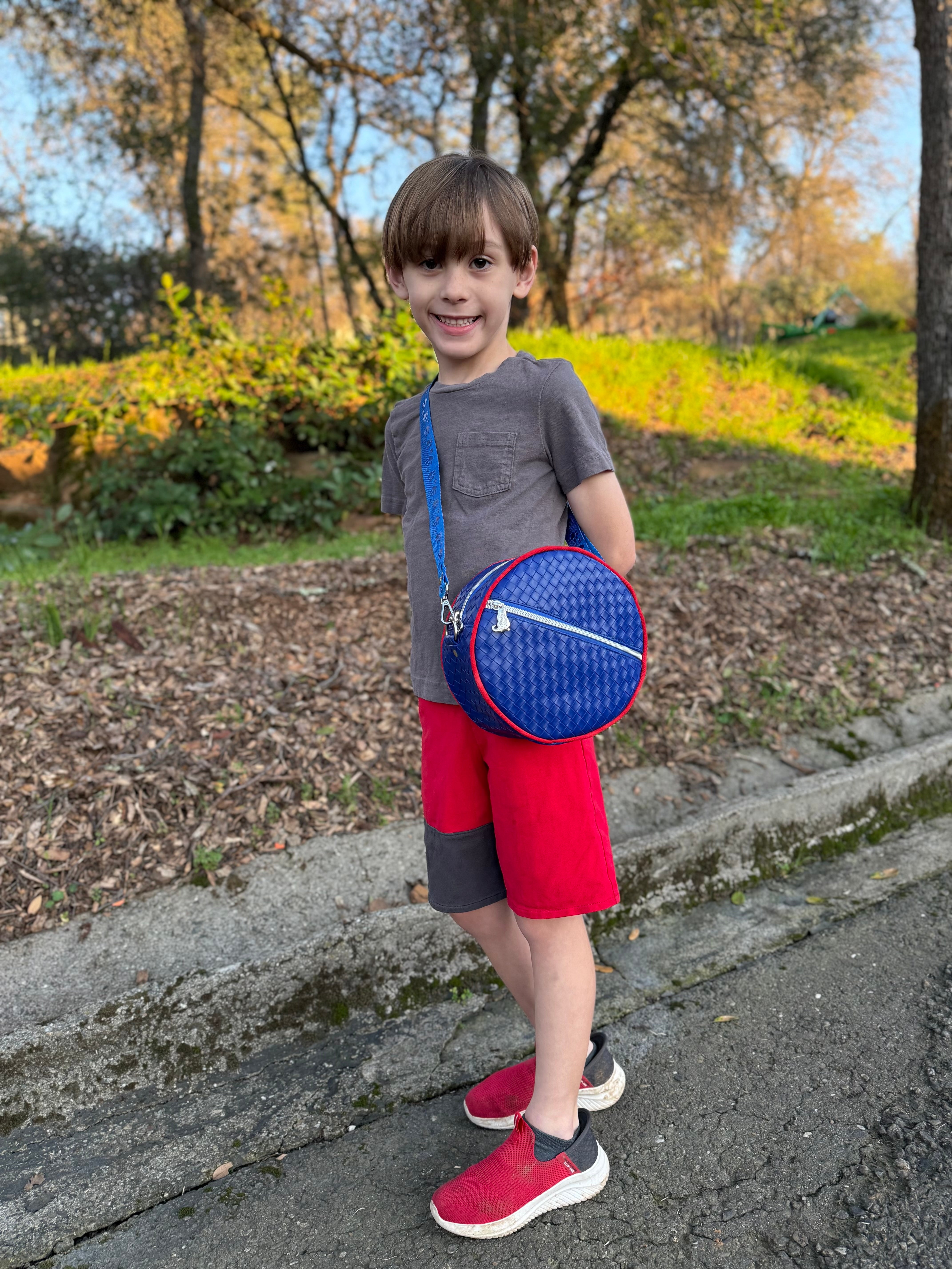 boy wearing the Small Ellie Round Bag in quilted vinyl blue fabric with a blue strap and red piping.