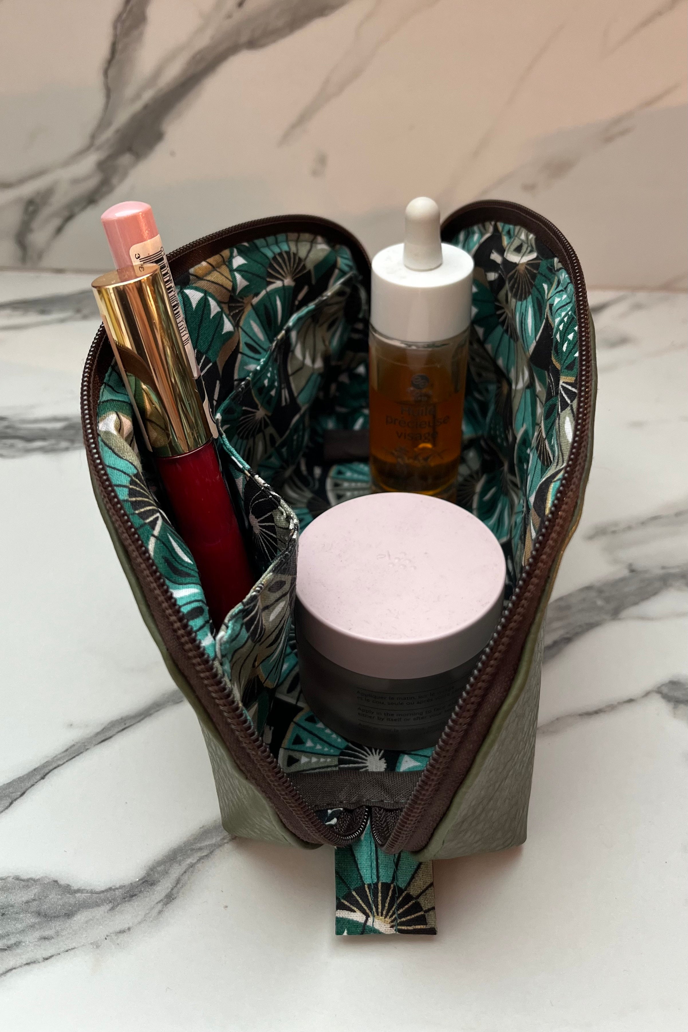 Makeup pouch with cosmetic items on a marble surface