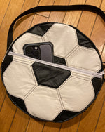Soccer ball-shaped bag with a phone inside on a wooden floor