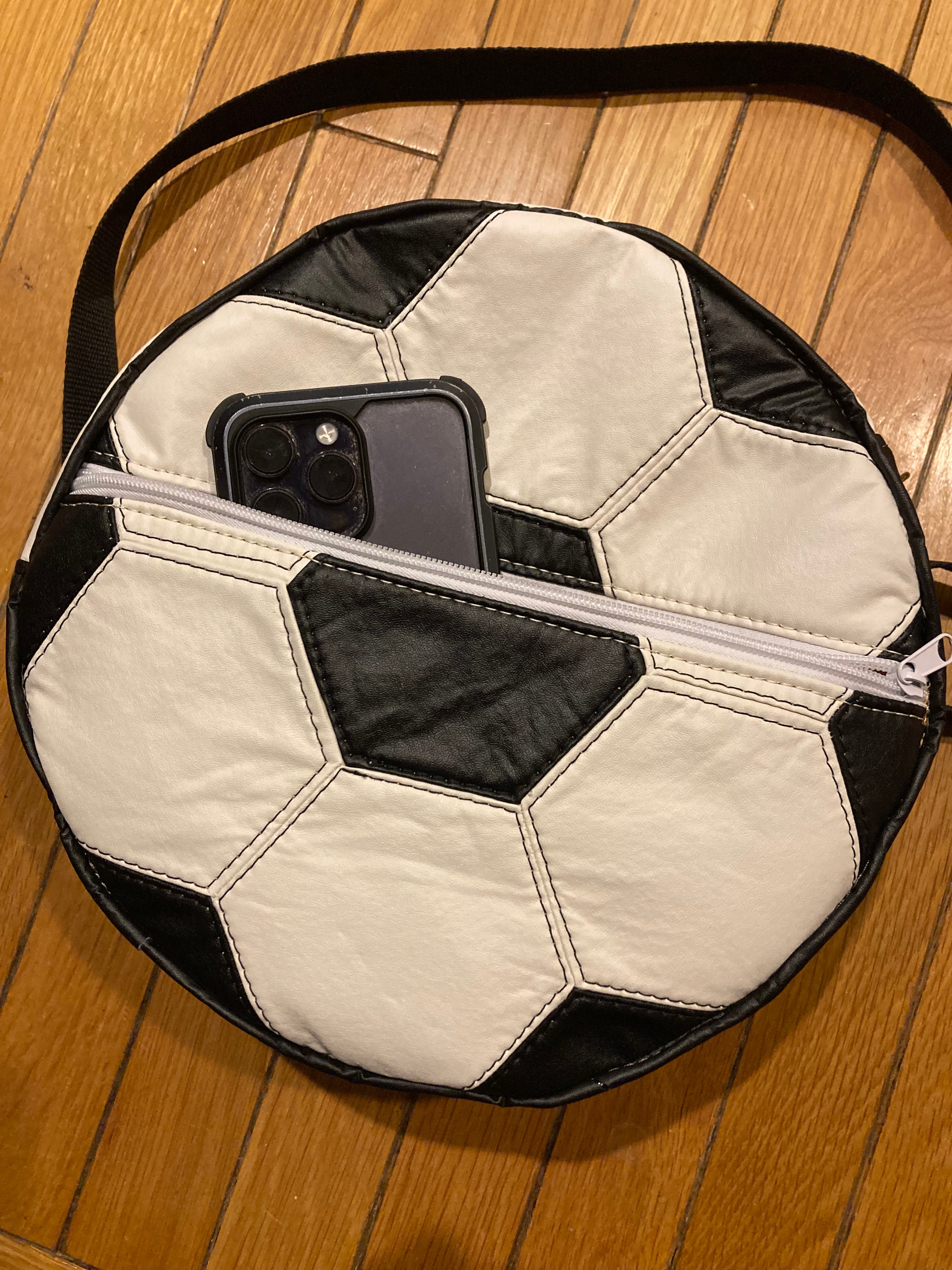 Soccer ball-shaped bag with a phone inside on a wooden floor
