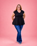 A woman modeling a black short-sleeve peplum top with blue jeans and blue sneakers, standing against a solid pink background. The top is made using Ellie and Mac PDF sewing patterns. They include A4, Letter, A0, and Projector pattern files. They also include a full sew-along tutorial. 