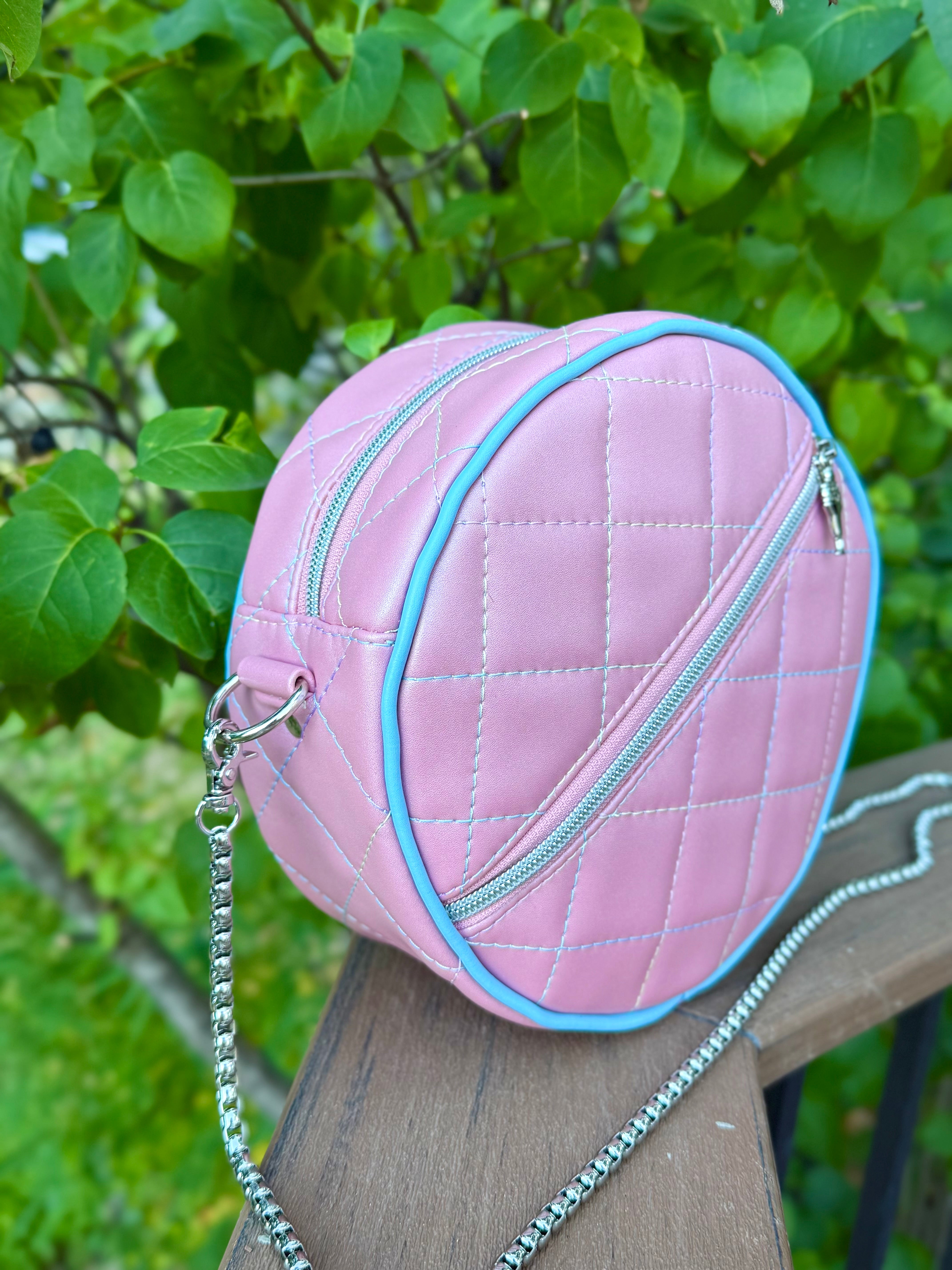 Pink quilted vinyl handbag with a chain strap on a wooden surface with green leaves in the background