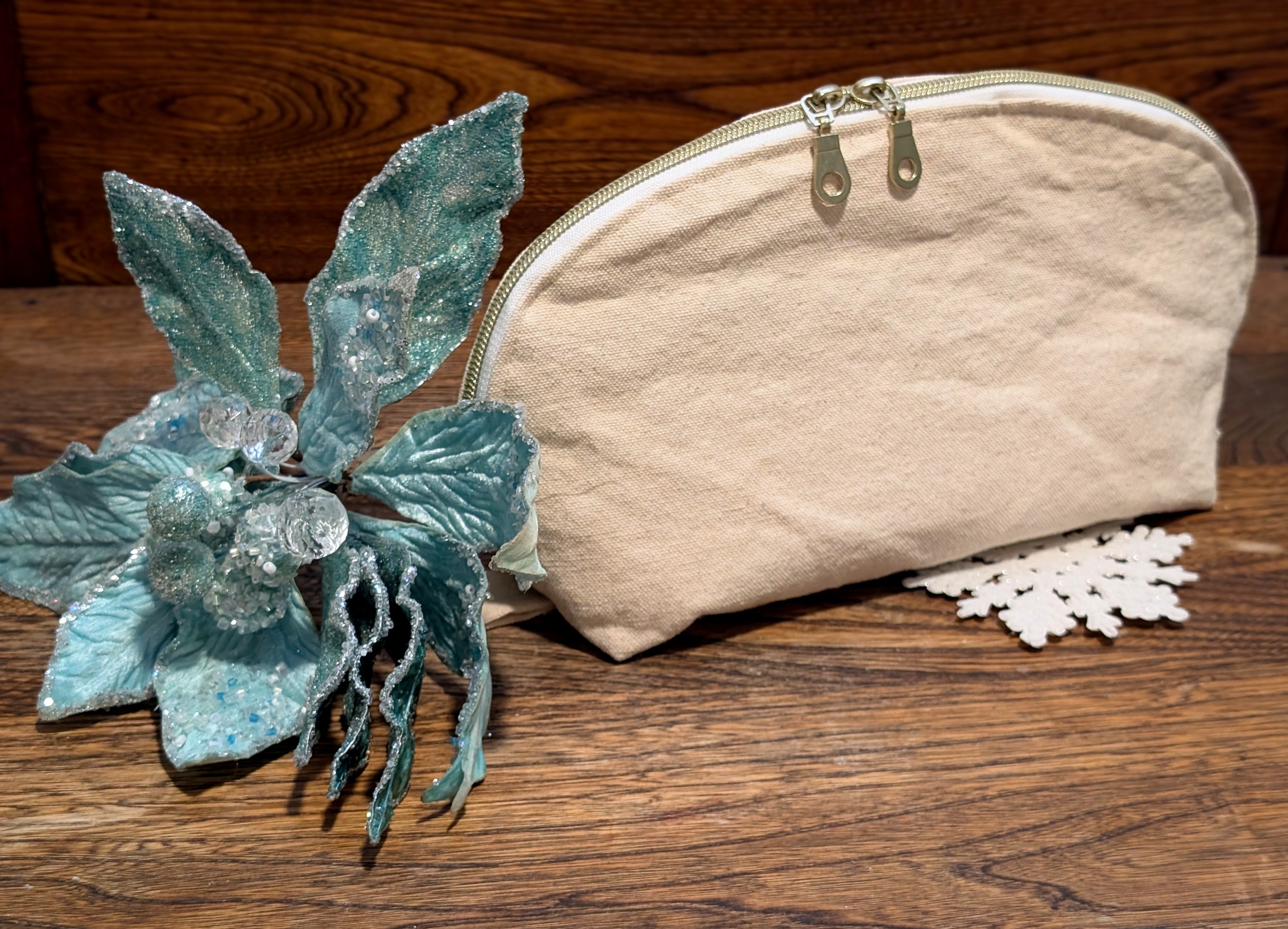 Beige makeup bag with decorative blue floral accessory on a wooden surface
