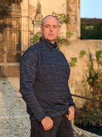 Man standing in front of an ancient building wearing a heathered navy fabric turtleneck sweater.