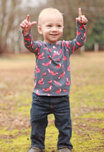 Little boy with a fox print fabric long sleeve henley top is standing in a field with his arms raised up.