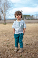 Boy with a striped fabric henley stands in a field with his hands in his pockets. Cute pocket detail and snap placket. Easy sewing pattern for knit fabrics.
