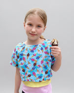 Young girl wearing a colorful ice cream patterned top holding a chocolate ice cream cone.