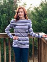 Women with red hair wearing a striped off shoulder sweater with slouchy cowl standing on a deck with trees in the background.