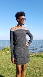 A tall woman with black short hair is standing in front of a beautiful body of water. The woman is wearing a cute sweater dress with banded, off shoulder neckline and curved hem. The dress is mid-thigh length.