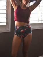 Woman standing indoors in front of a window wearing a burgundy tank top and high rise floral panties Sewn using the Feel Frisky Panties sewing pattern by Ellie and Mac sewing patterns. Perfect for beginners and includes projector file, A0 copy shop file, A4 and Letter pattern print file, and full video sew along tutorial. 
