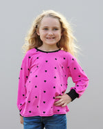 Young girl wearing a pink long-sleeve shirt with black heart patterns against a gray background