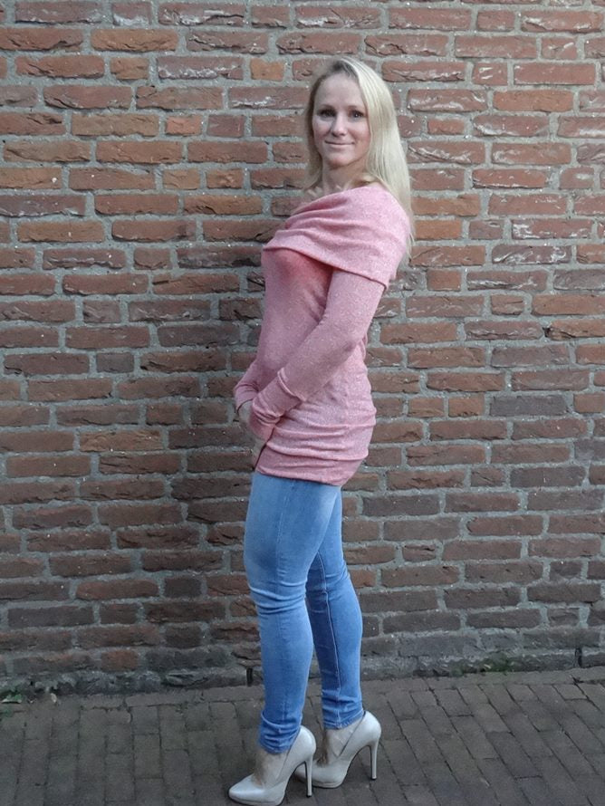 Woman in a sexy pink sweater with long sleeves and oversized cowl off shoulder neckline. She is wearing skinny jeans and heels. 
