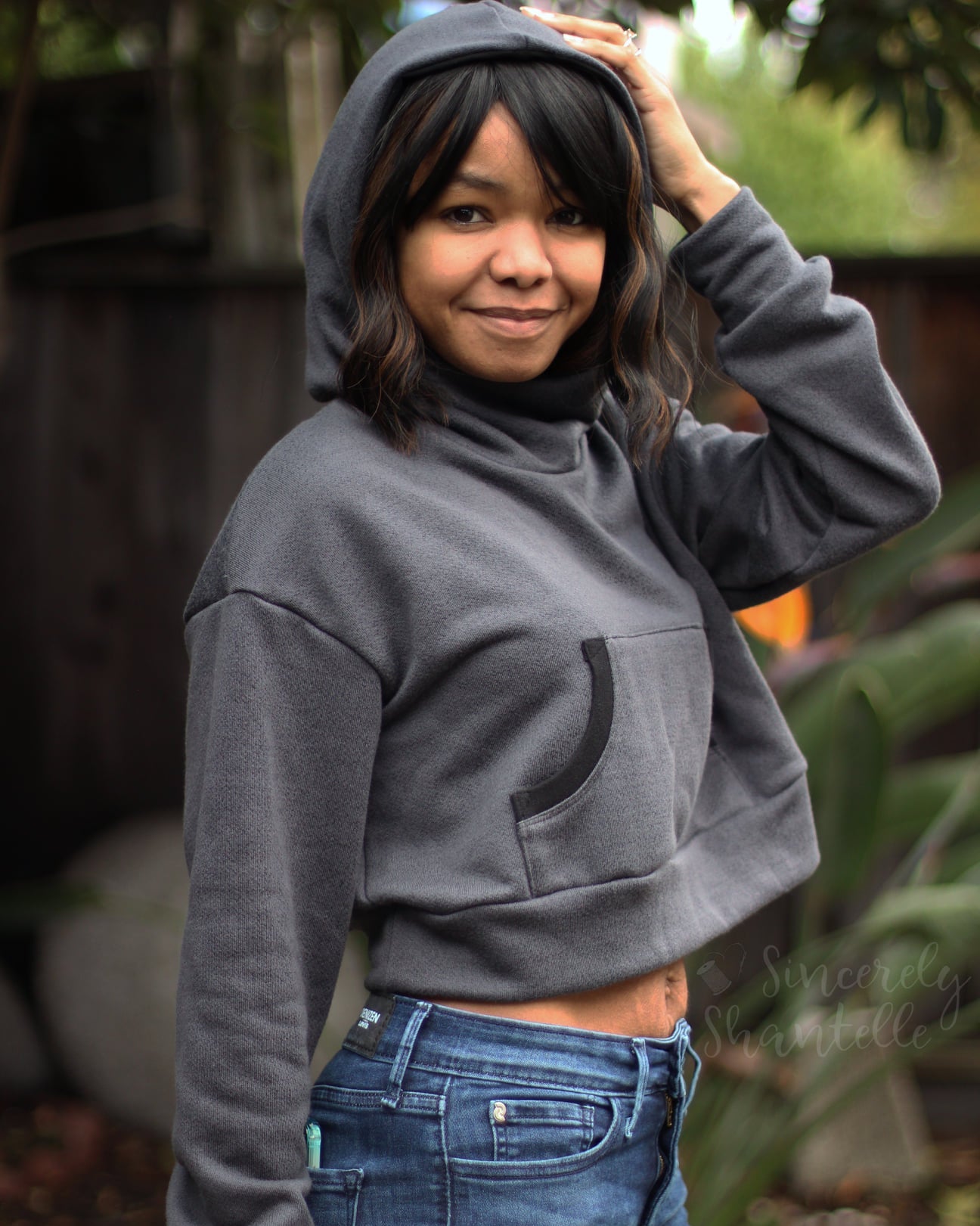 Woman wearing a grey oversized sweatshirt with hood and kangaroo pocket.