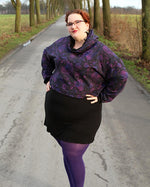 Woman wearing a purple sweater with cowl neck paired with a black skirt and purple stockings. 