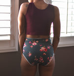 Woman standing in front of a window inside, wearing a burgundy tank top and floral high-rise panties Sewn using the Feel Frisky Panties sewing pattern by Ellie and Mac sewing patterns. Perfect for beginners and includes projector file, A0 copy shop file, A4 and Letter pattern print file, and full video sew along tutorial. 