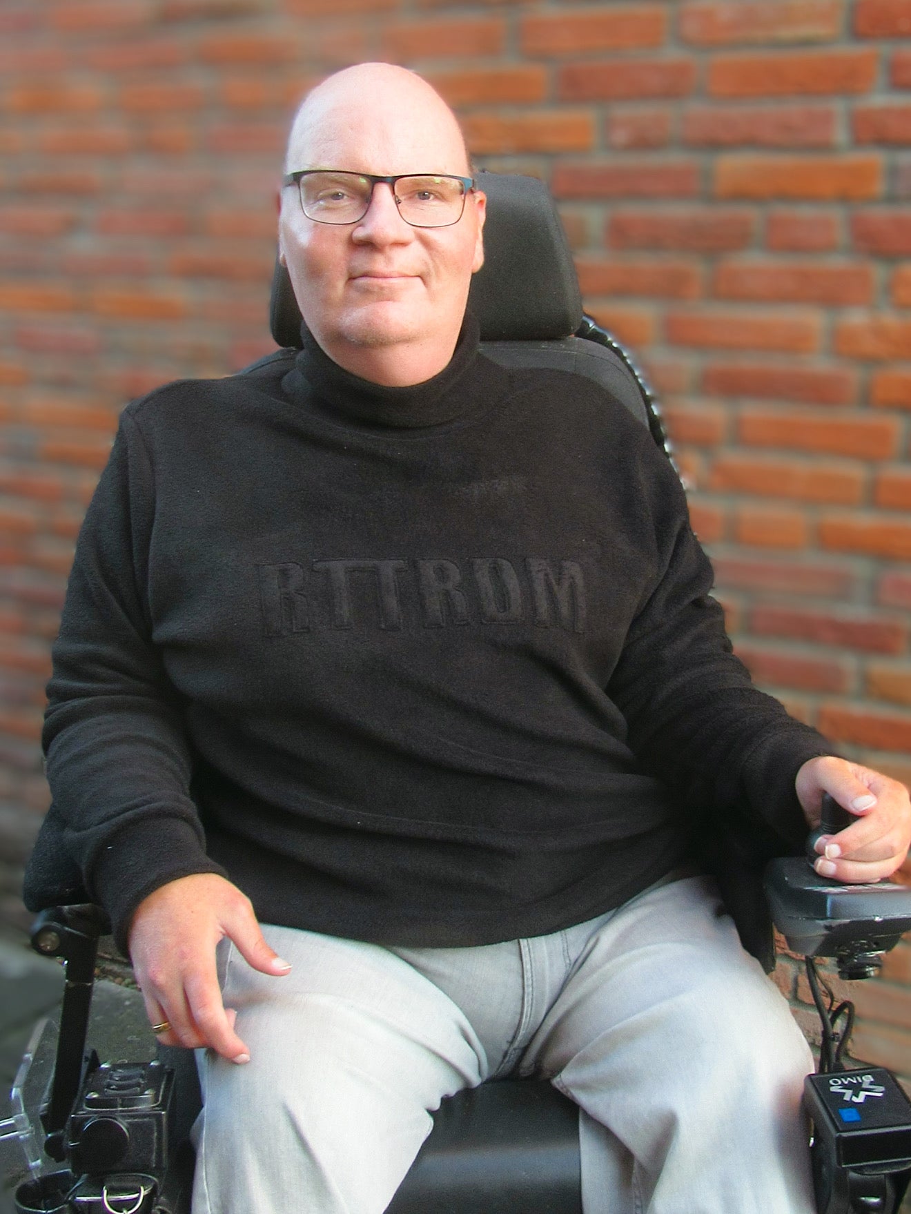 Man wearing a black turtleneck sweater made using Ellie and Mac sewing patterns sitting in a wheelchair in front of a brick wall.