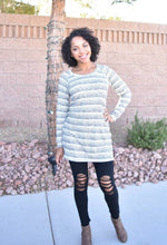 Women wearing a cozy striped raglan sweater with black ripped skinny jeans and booties. 